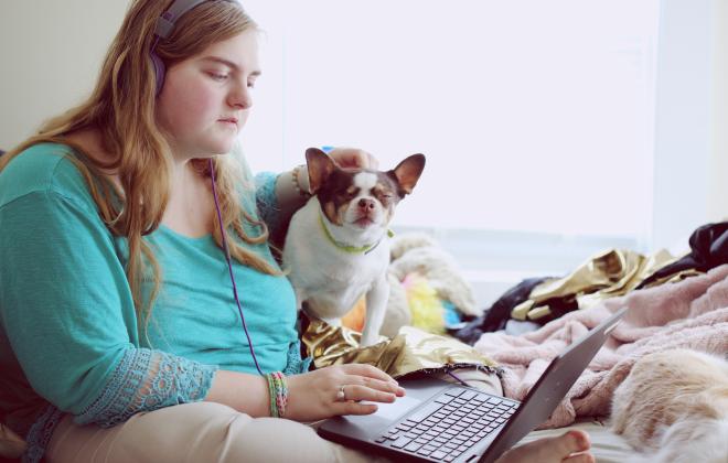 a young woman sitting with a dog typing on a laptop computer